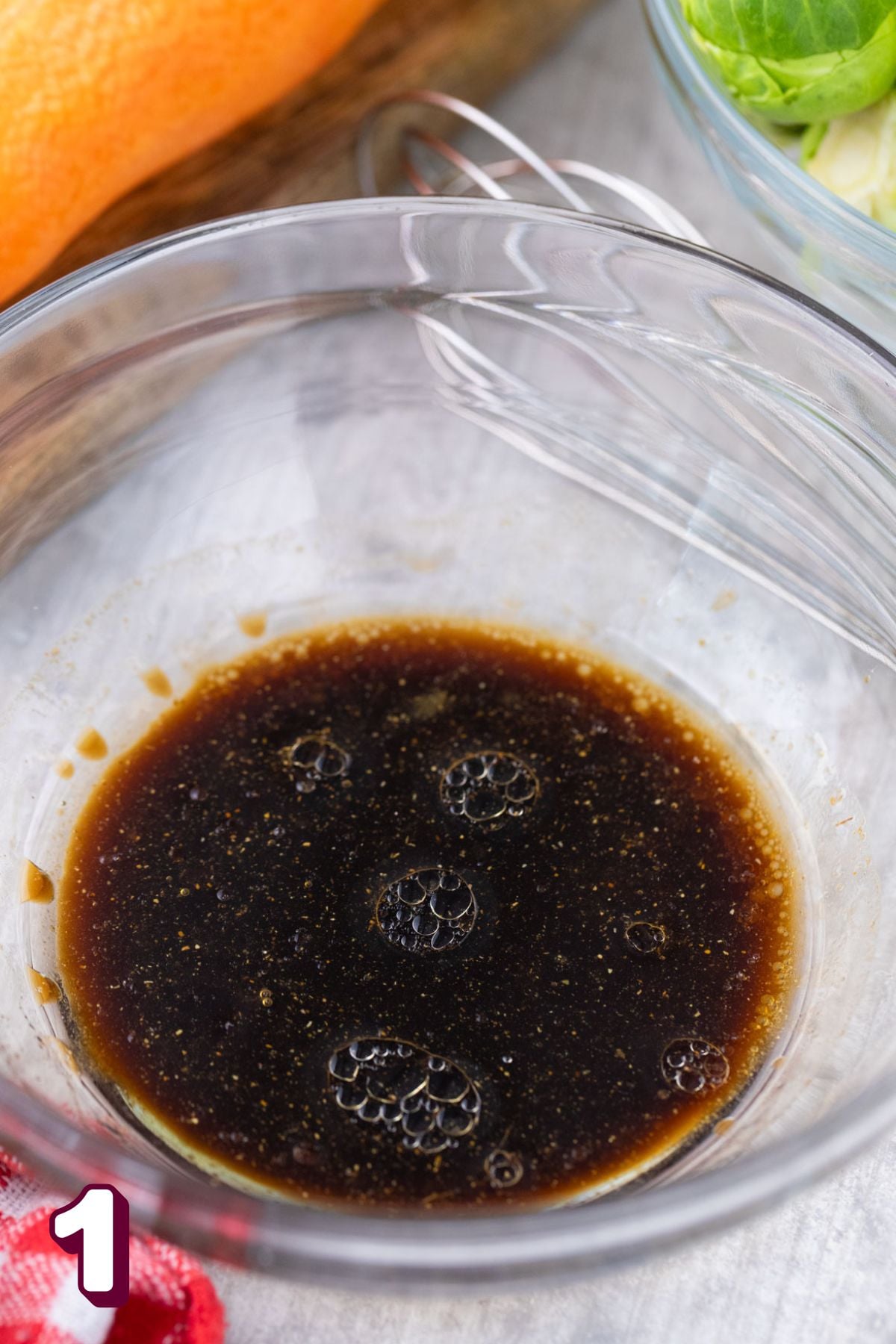 Maple balsamic dressing in a bowl with a whisk behind it.