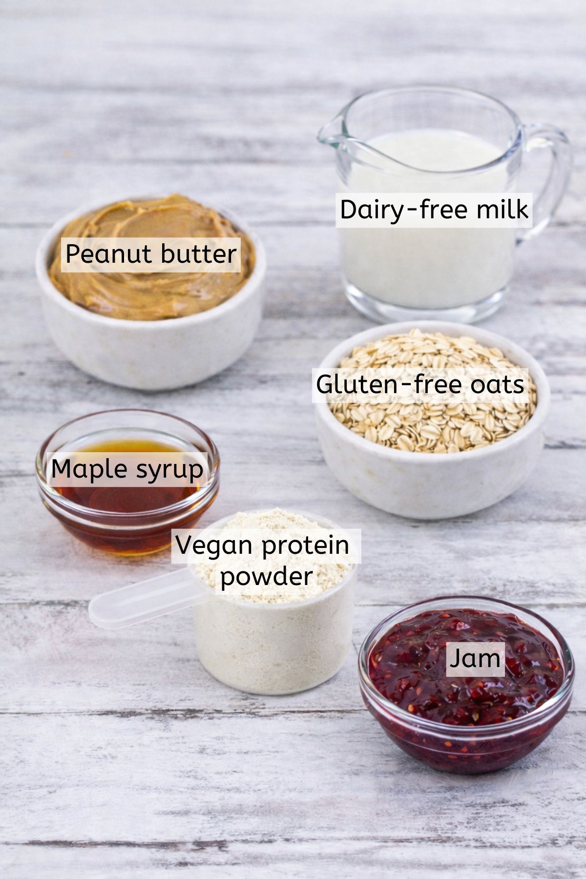 Rolled oats, protein, jam, syrup, and milk all in bowls with text labels over top.