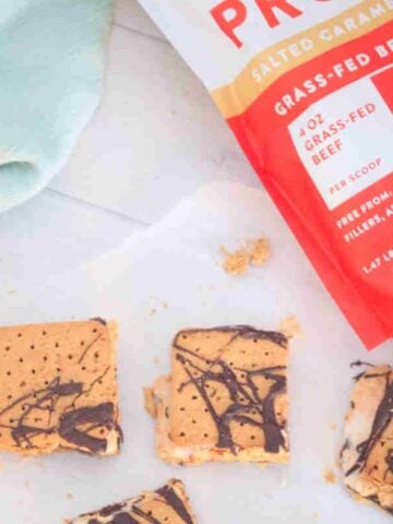 Frozen protein s'mores on parchment paper with a protein powder behind it.