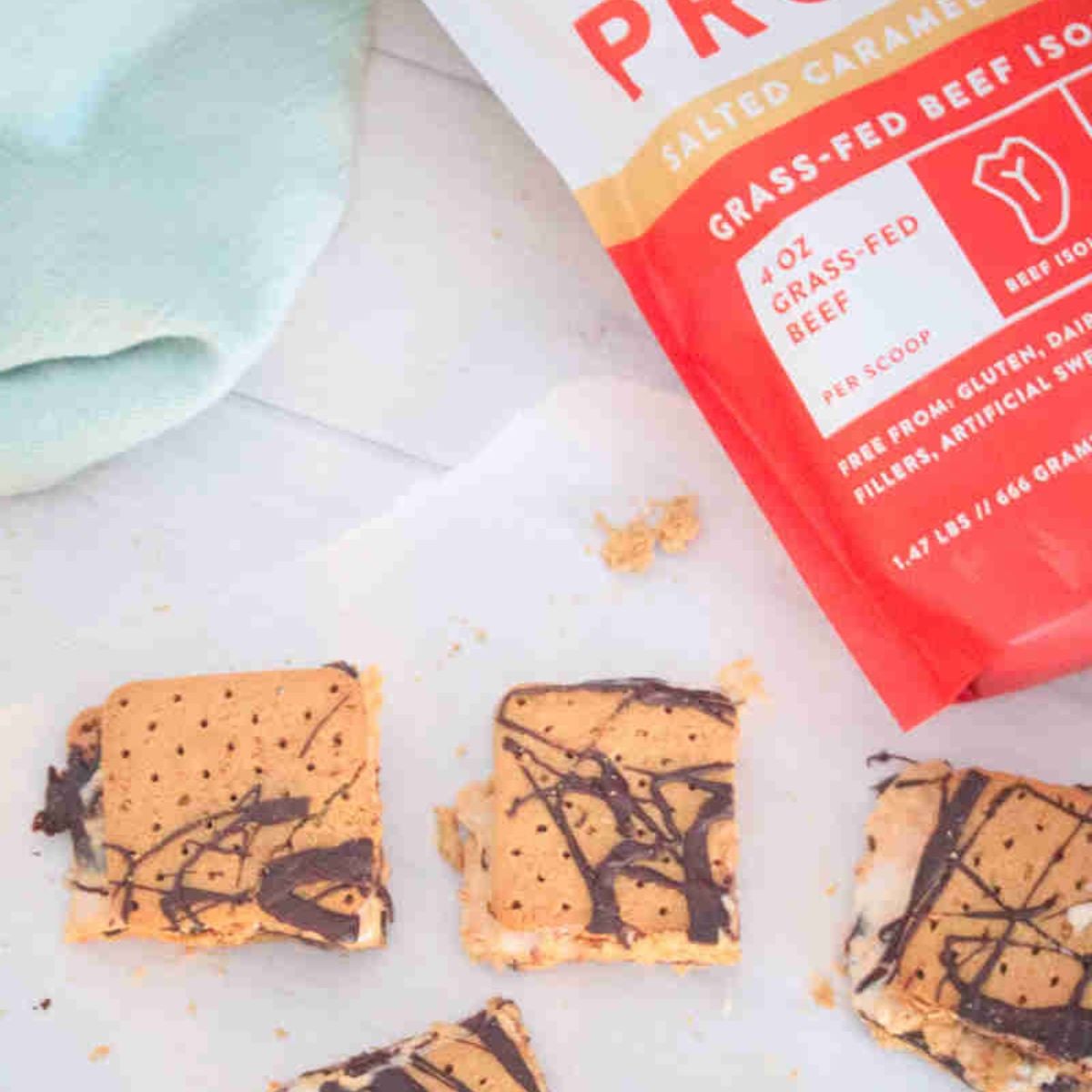 Frozen protein s'mores on parchment paper with a protein powder behind it.