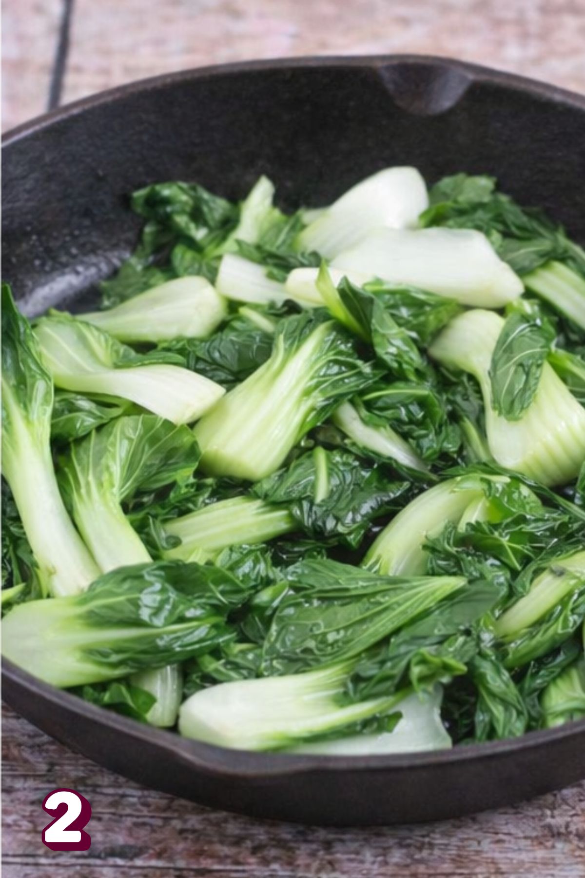 Bok choy being sauteed in a cast iron pan.