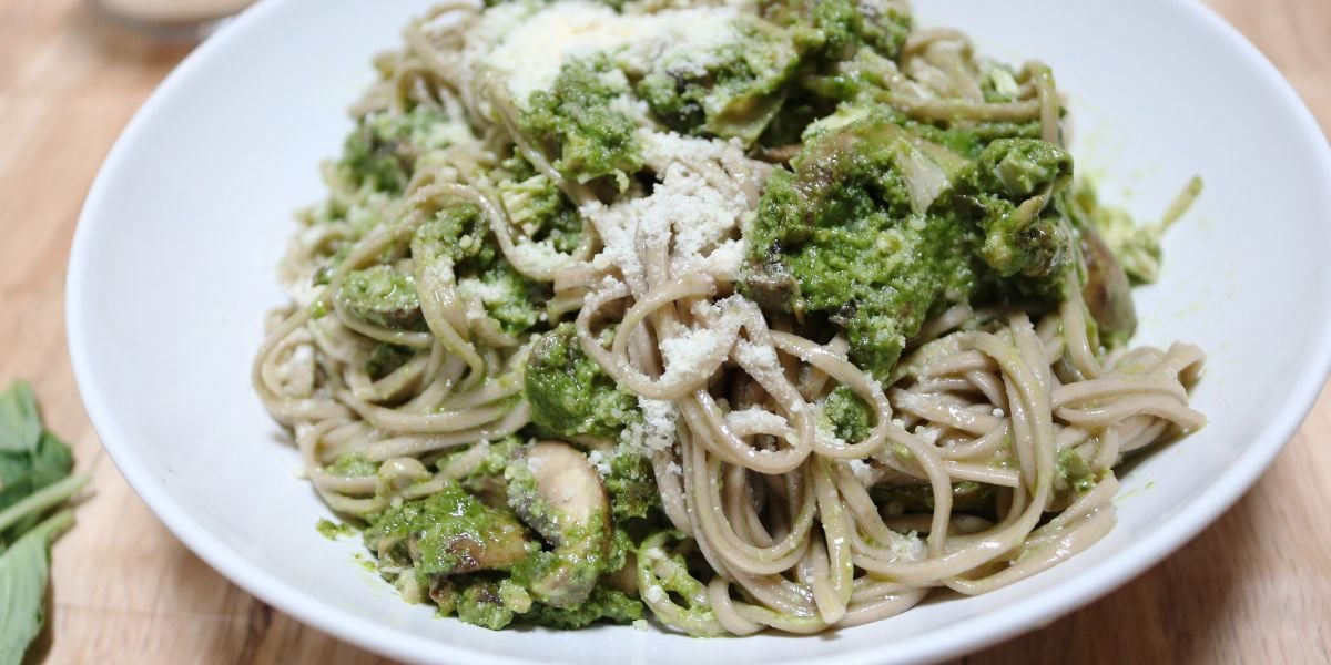 Chicken pesto pasta with mushrooms in a white bowl.
