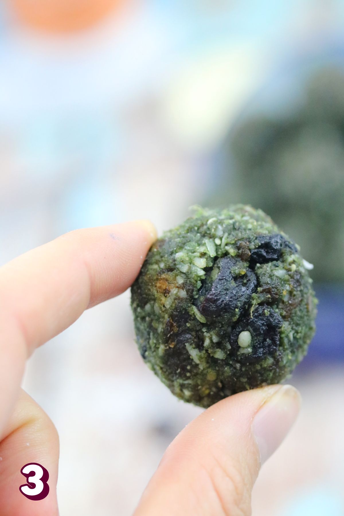 Two fingers holding up a spirulina energy ball.