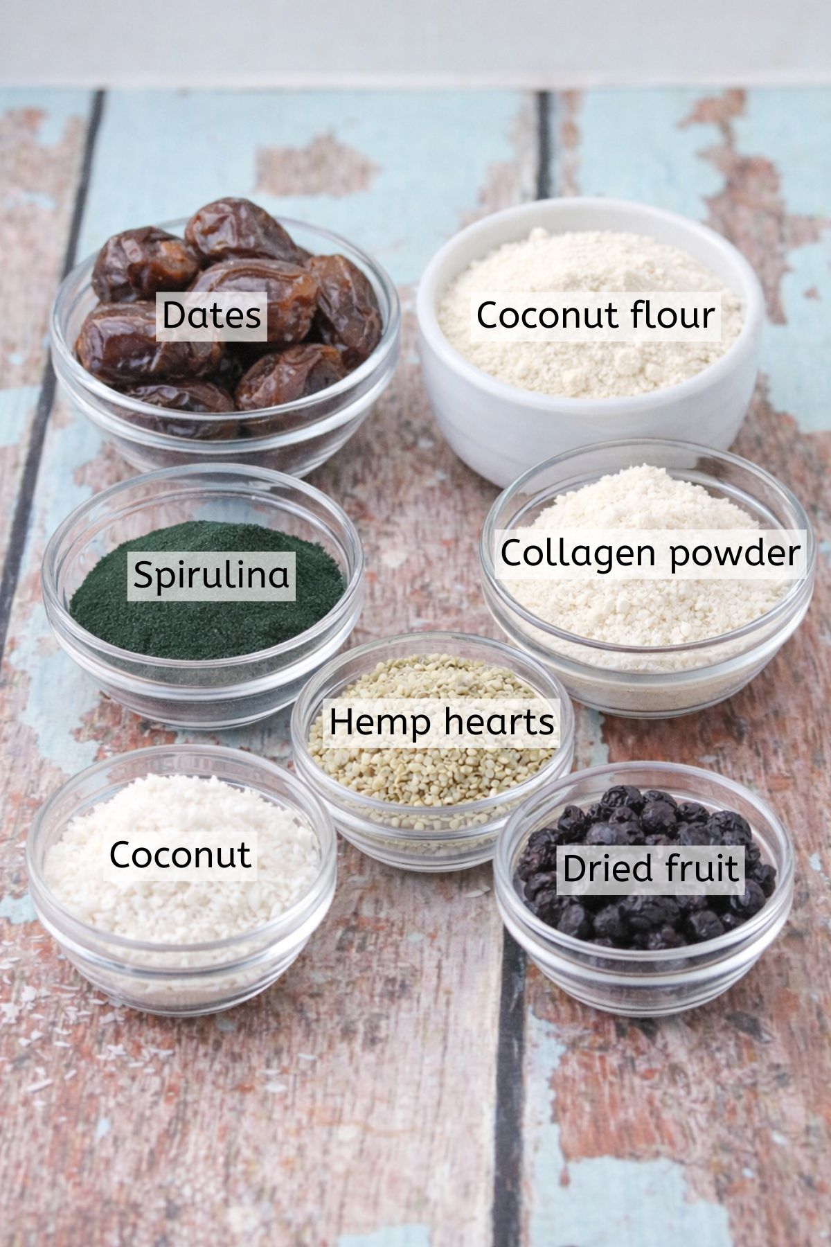 Coconut, spirulina, dates, dried fruit and more in glass bowls with text labels over top.