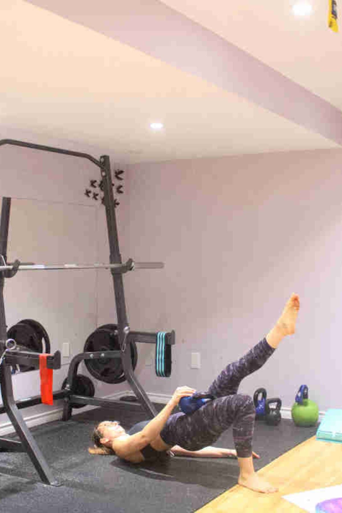 Woman performing a single leg glute bridge with a kettlebell on her hip.