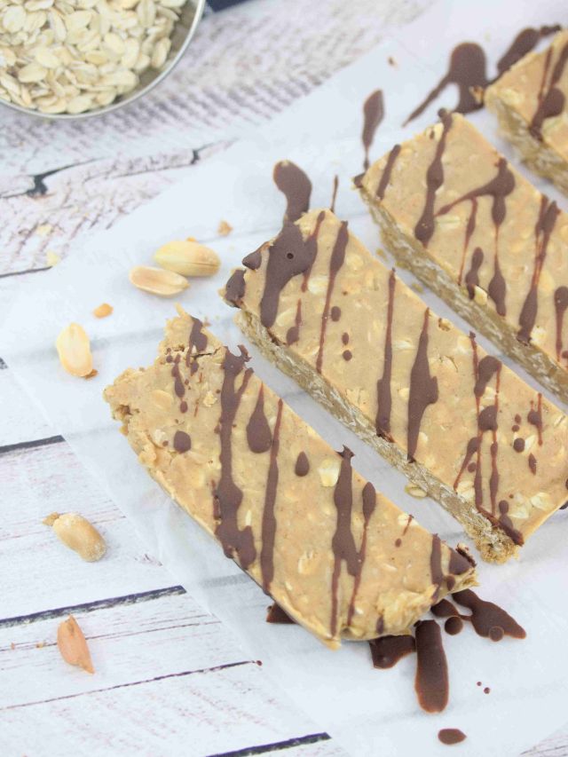 Five peanut butter vanilla protein bars lined up flat on parchment paper and drizzled with chocolate.