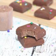 Chocolate protein powder fudge stacked with a bite out of one piece and more pieces behind them.
