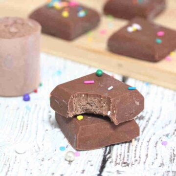 Chocolate protein powder fudge stacked with a bite out of one piece and more pieces behind them.