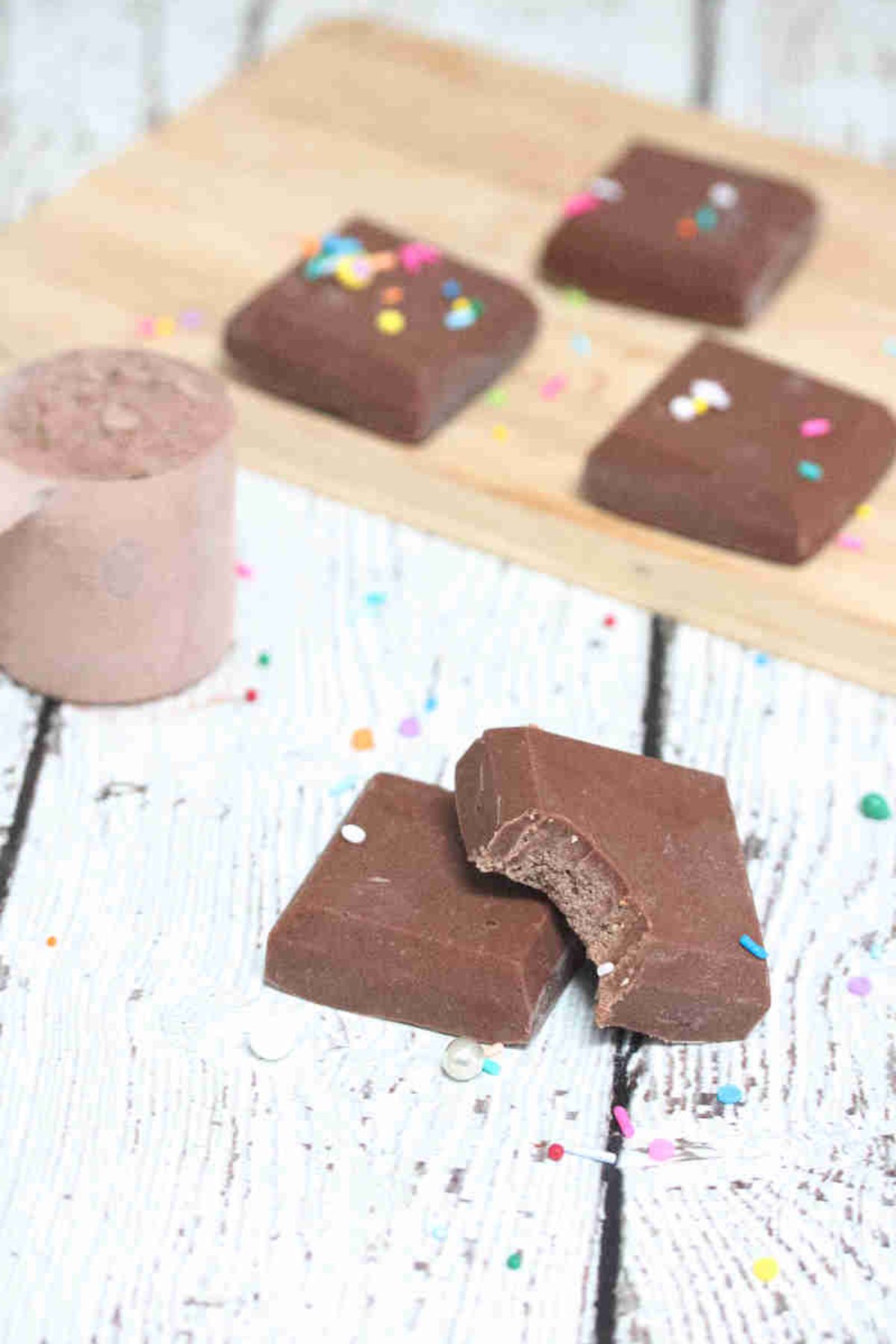 Chocolate protein powder fudge stacked with a bite out of one piece and more pieces behind them.