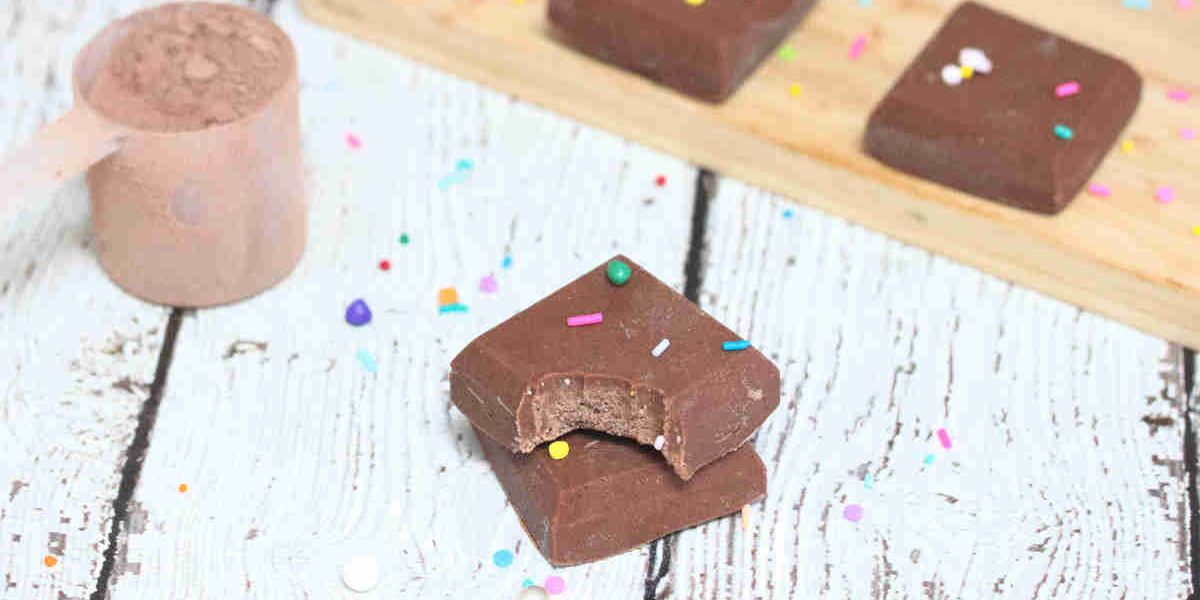 Chocolate protein powder fudge stacked with a bite out of one piece and more pieces behind them.