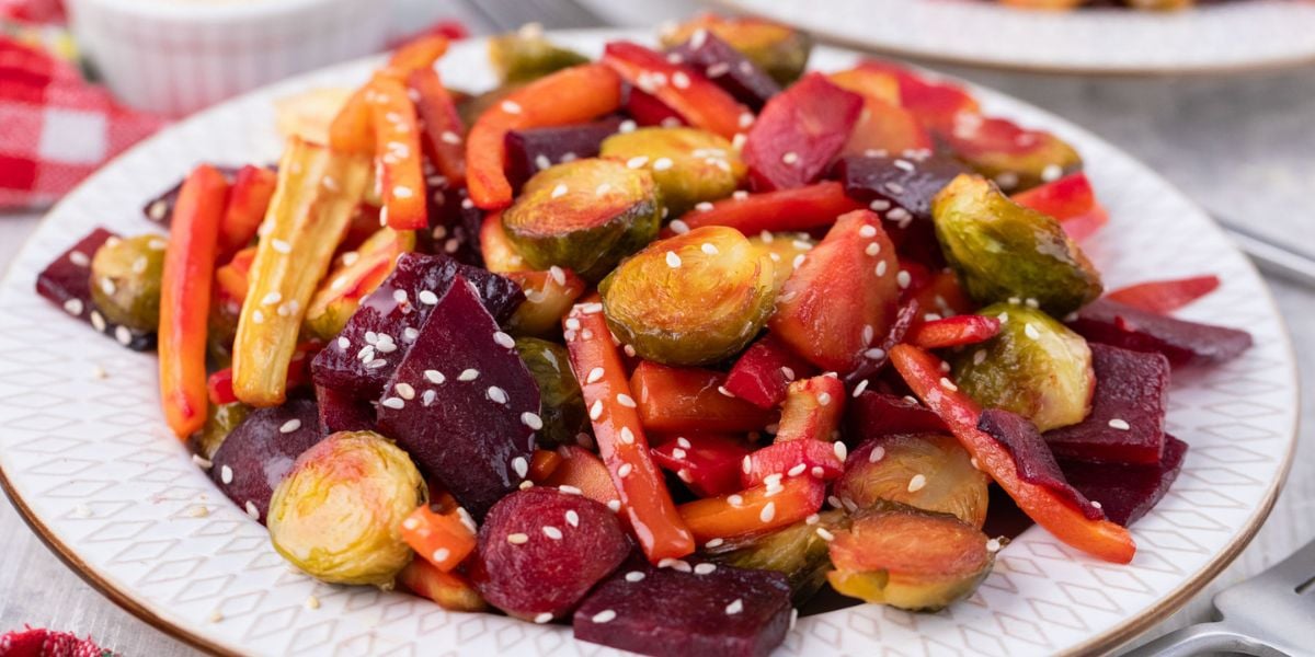 Roasted Brussels, carrots, and beets on a plate with sesame seeds.