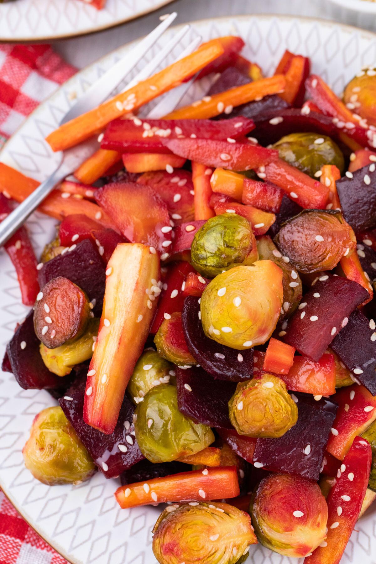 Roasted Brussels, carrots, and beets on a plate with sesame seeds.