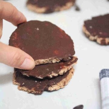 Three beef protein powder cookies with chocolate stacked with two fingers holding the top cookie.