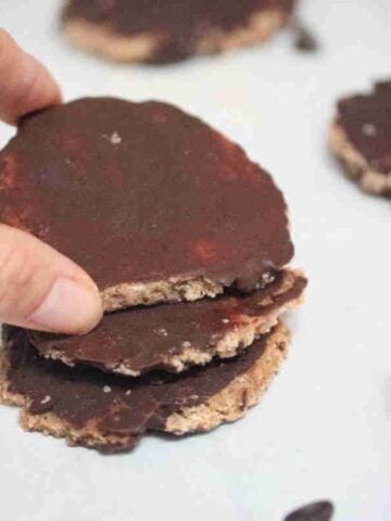 Three beef protein powder cookies with chocolate stacked with two fingers holding the top cookie.