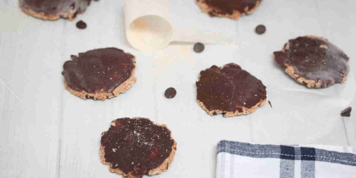 Chocolate topped protein powder cookies on parchment paper with chocolate chips around them.
