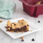 Square of protein blondies on a white plate with chocolate chips around it.