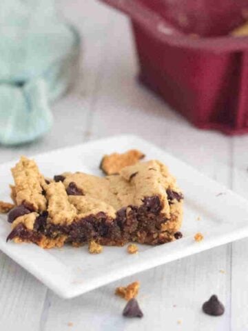 Square of protein blondies on a white plate with chocolate chips around it.