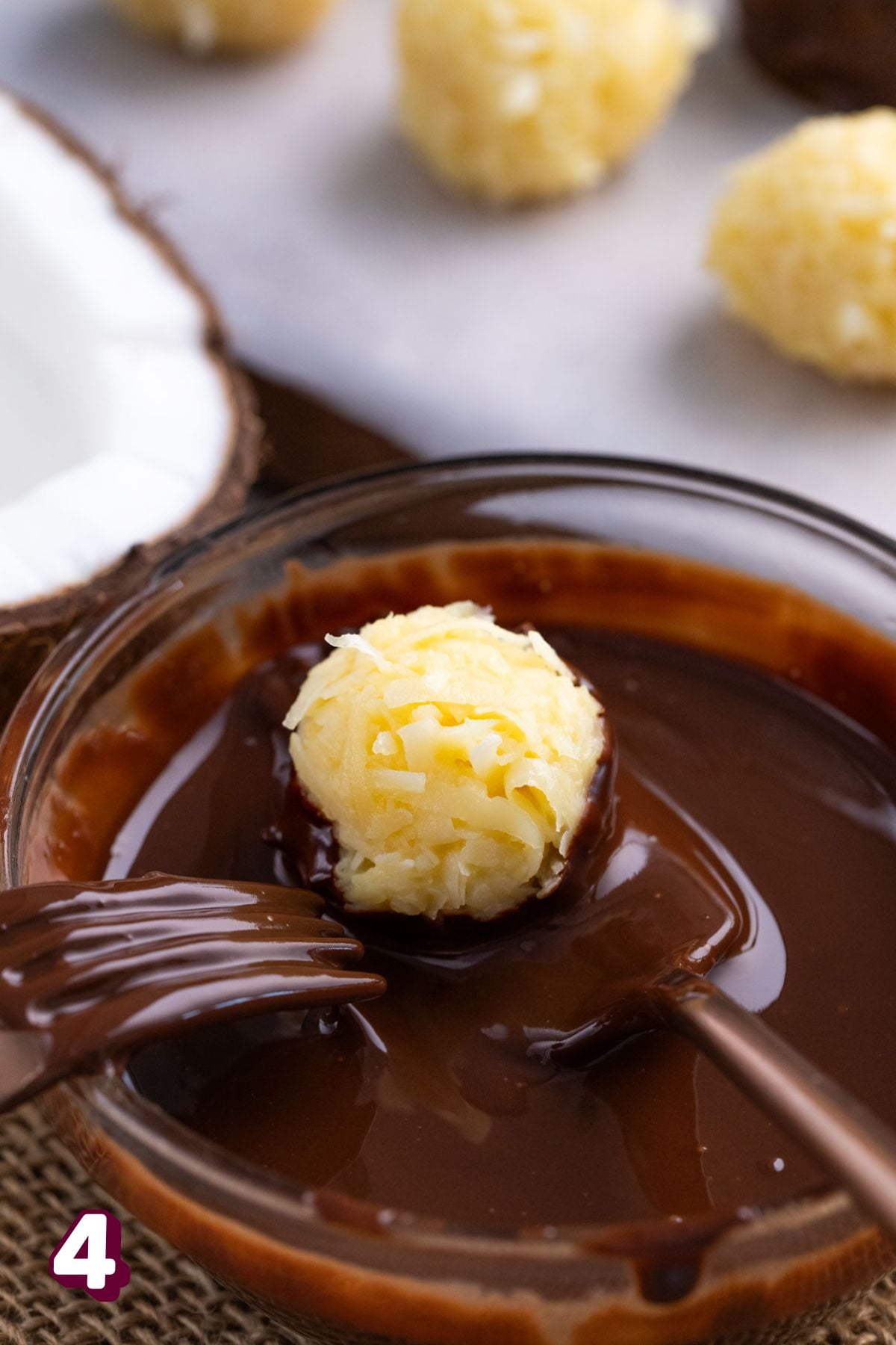 Coconut protein ball being dipped into chocolate.