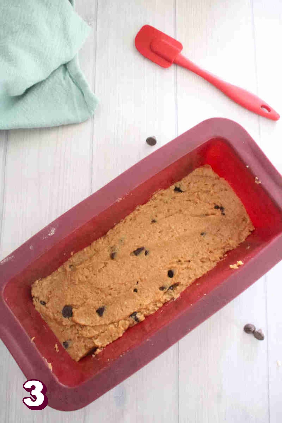 Uncooked protein blondies in a red silicone loaf pan.