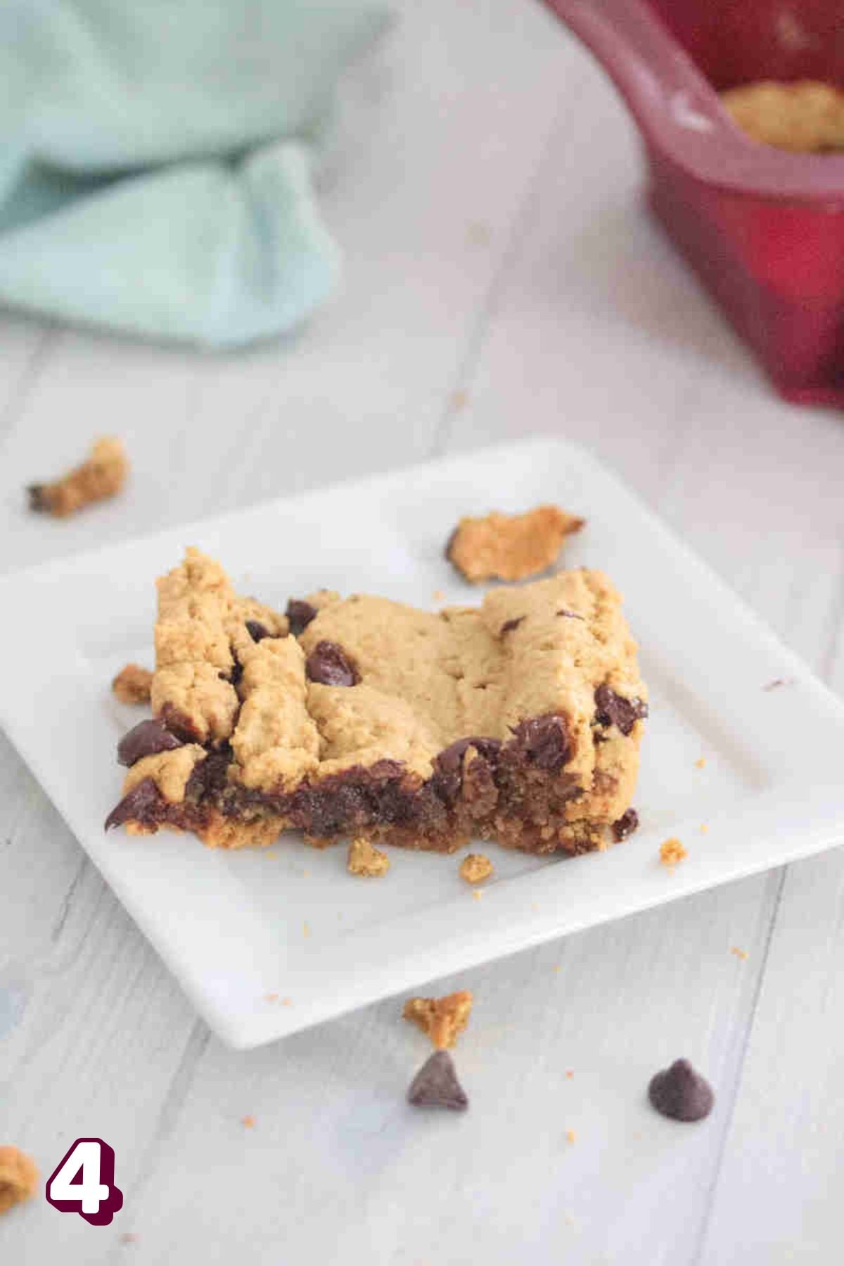 Square of protein blondies on a white plate with chocolate chips around it.