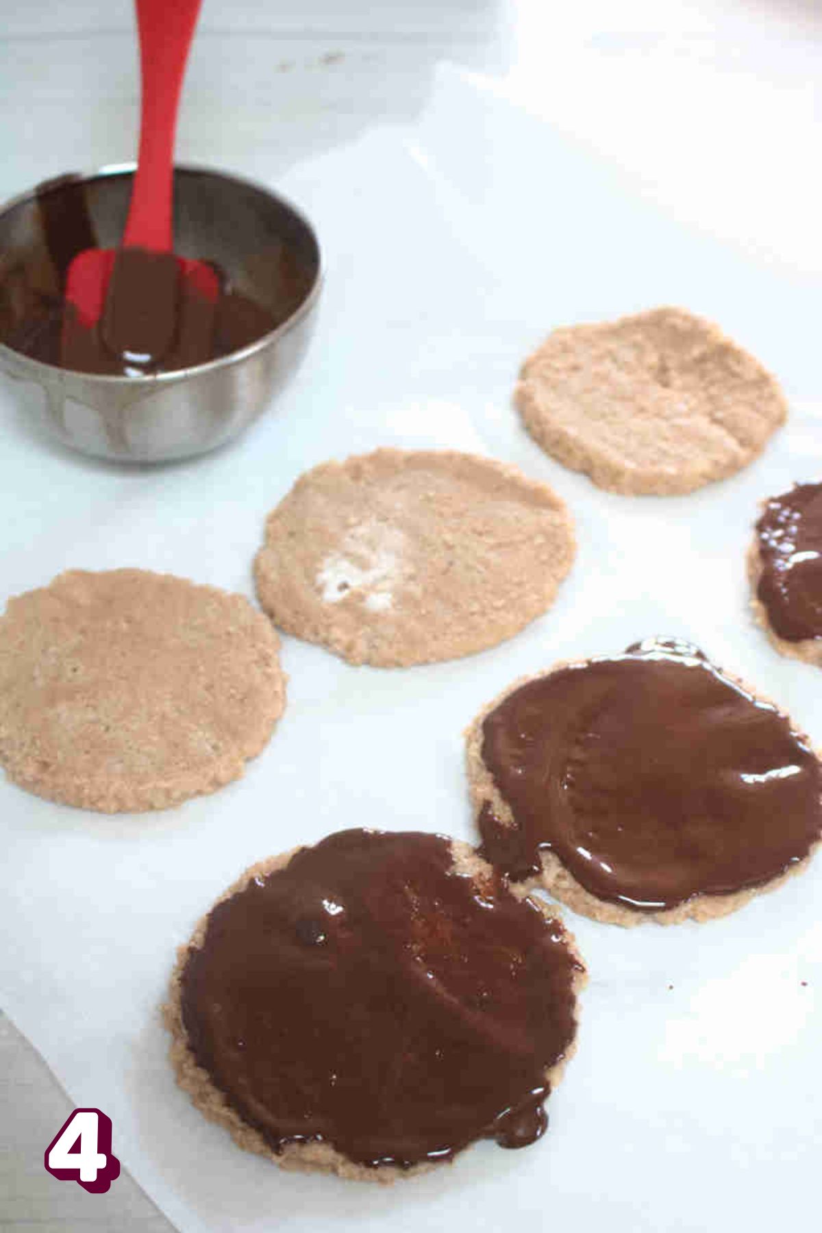 Protein thin mints on parchment paper being painted with chocolate.