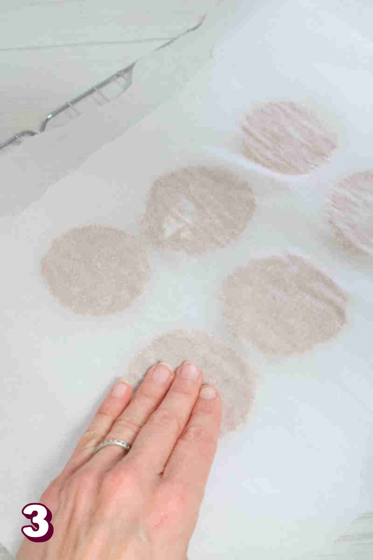 Hand pressing cookie dough balls flat under a piece of parchment paper.