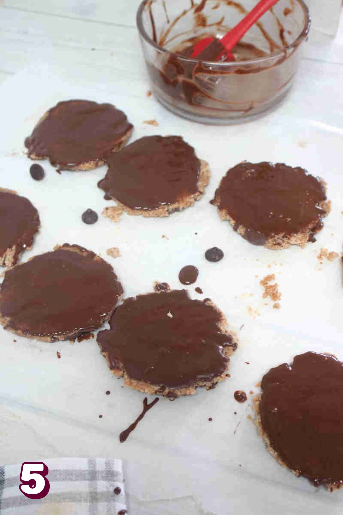 Protein thin mints on parchment paper being painted with chocolate.
