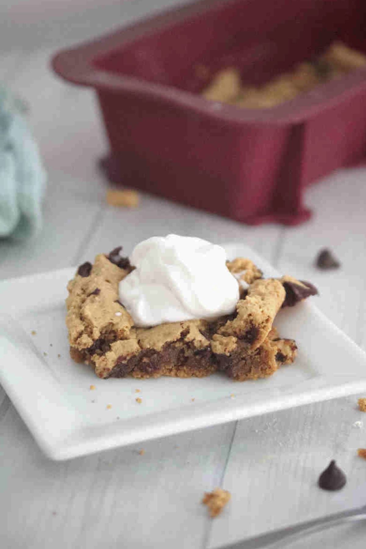 Square of protein blondies on a white plate with coconut whip on top and chocolate chips around it.