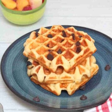 Blue plate with three chocolate chip blender waffles on it and fruit behind the plate.