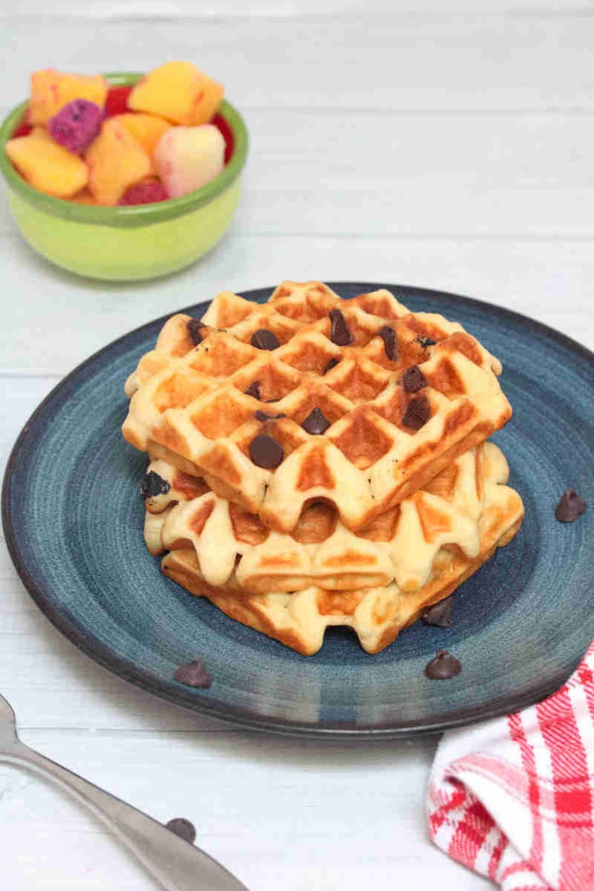 Blue plate with three chocolate chip blender waffles on it and fruit behind the plate.