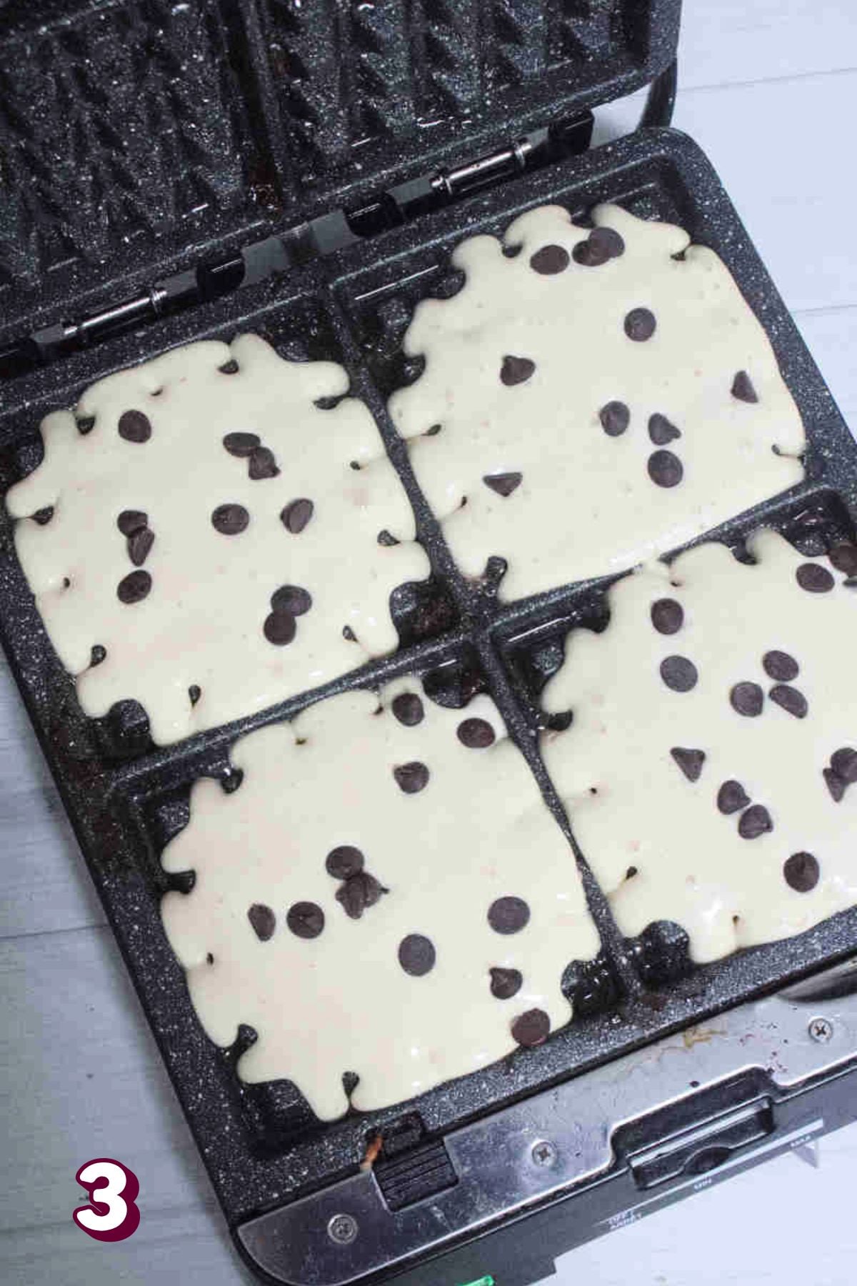 Cast iron waffle pan with raw chocolate chip waffle batter in it.