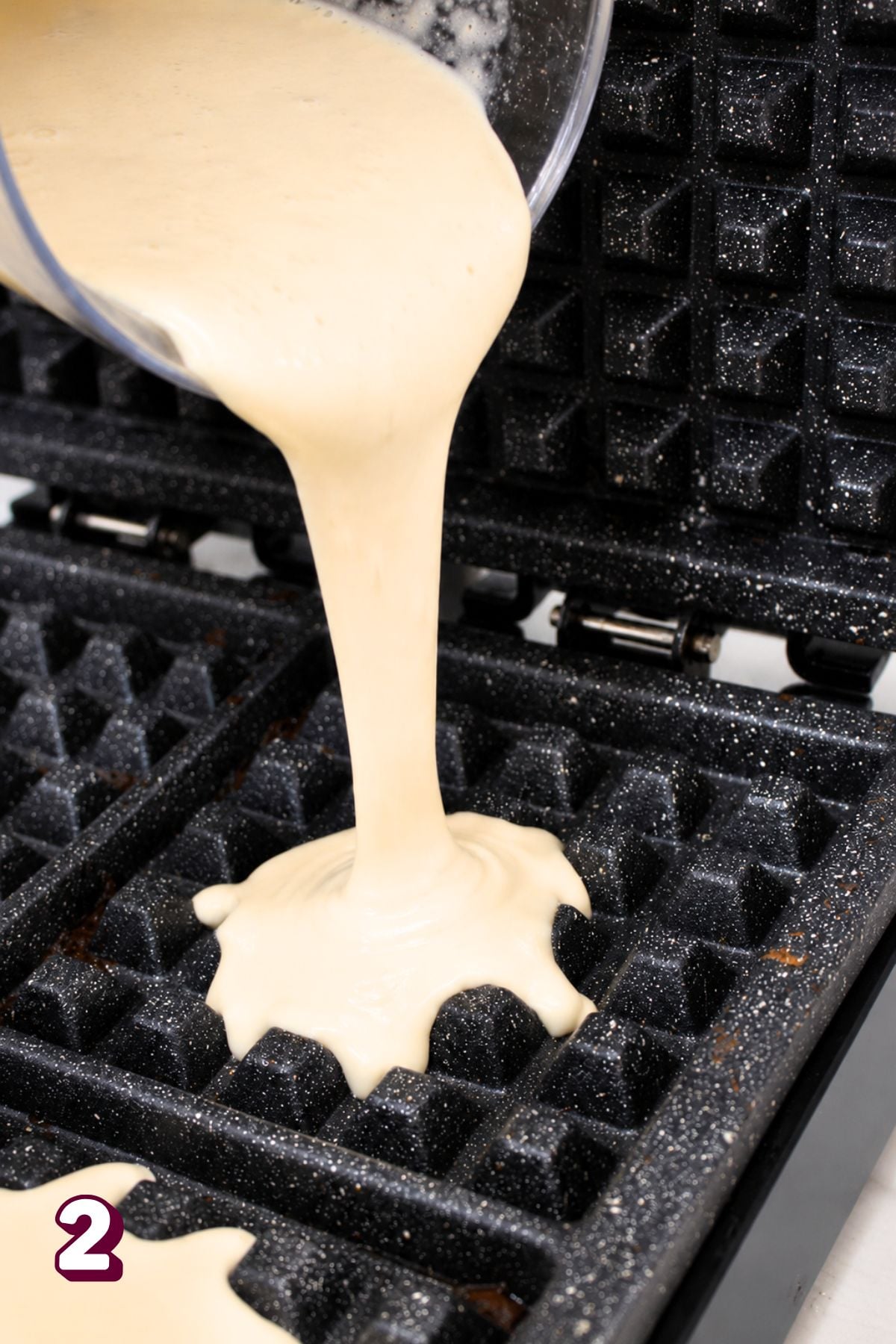 Blender waffle batter being poured into a cast iron waffle iron.