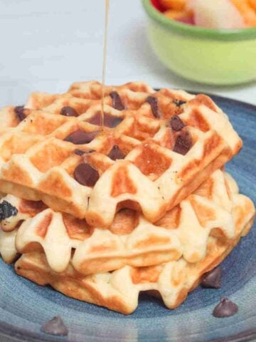Chocolate chip waffles with syrup being poured on them on a blue plate.