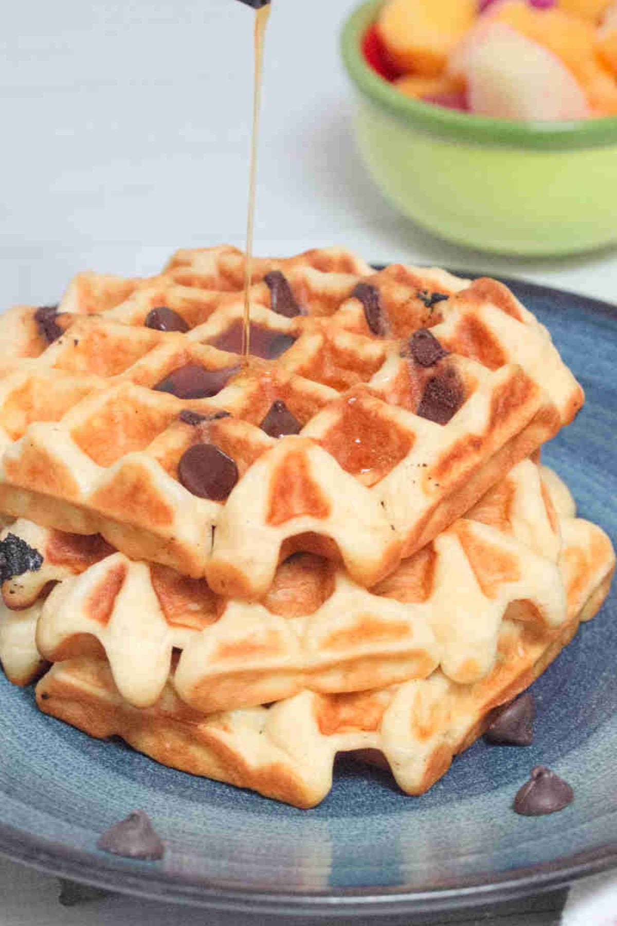 Chocolate chip waffles with syrup being poured on them on a blue plate.