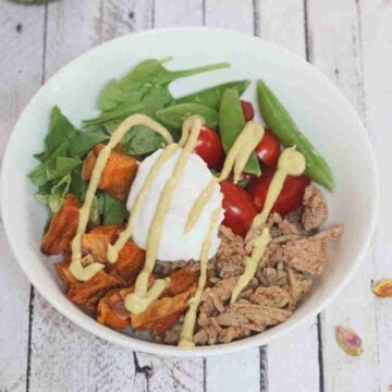 White bowl with ground meat, yogurt, veggies, and sweet ptoatoes.