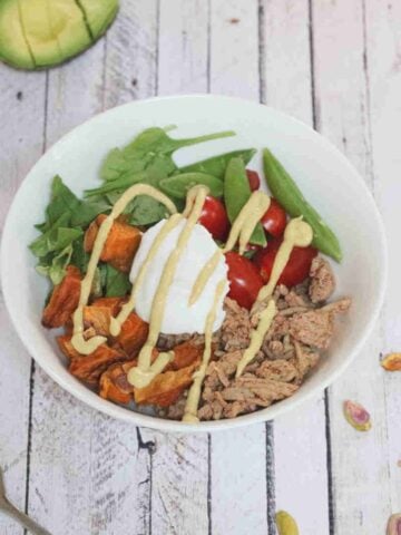 White bowl with ground meat, yogurt, veggies, and sweet ptoatoes.