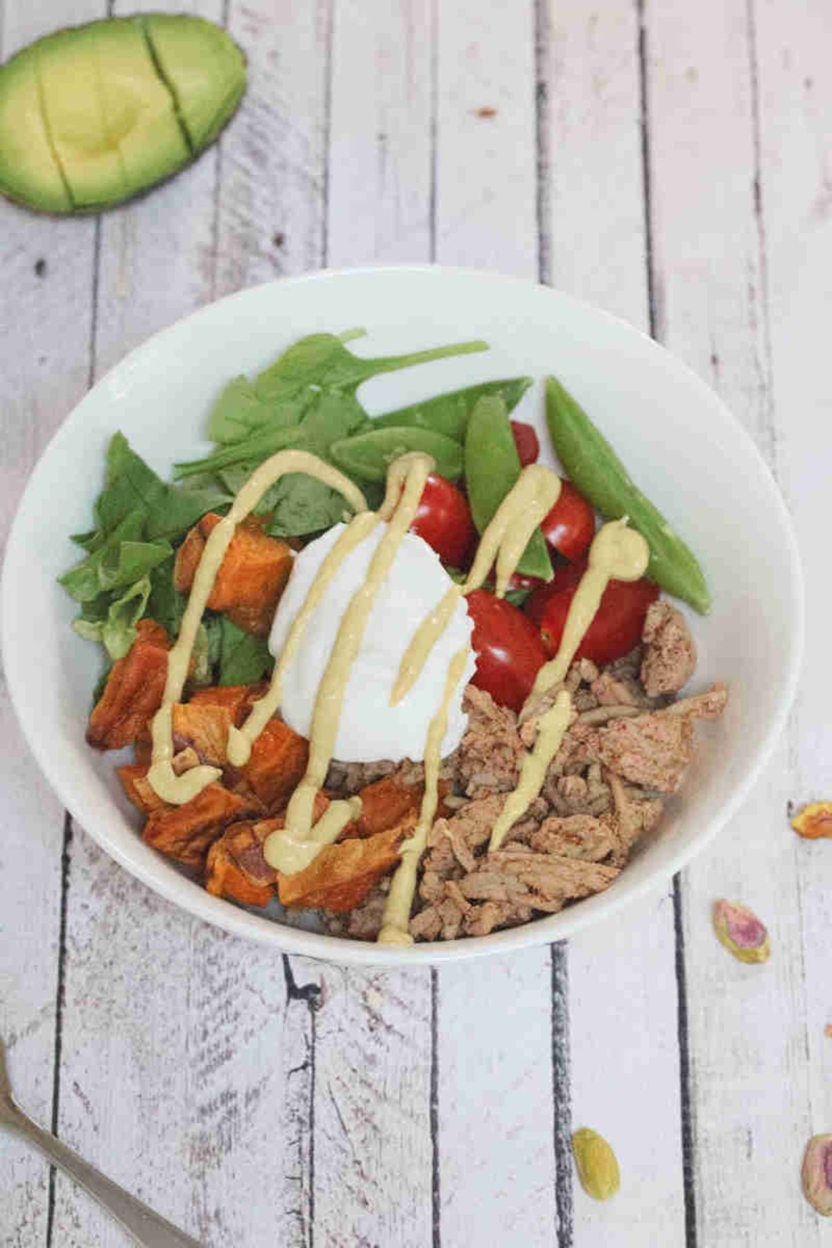 White bowl with ground meat, yogurt, veggies, and sweet ptoatoes.