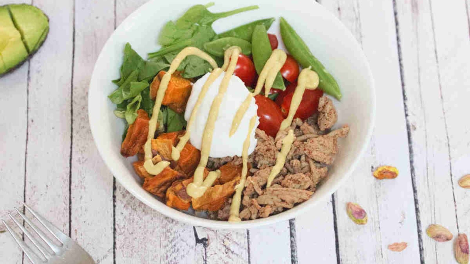 White bowl with ground meat, yogurt, veggies, and sweet ptoatoes.