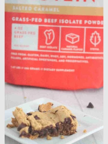 Protein blondie on a white plate with a bag of protein powder behind it.