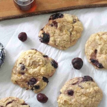 High-protien muffin tops with cherries on parchment paper with cherries around them.