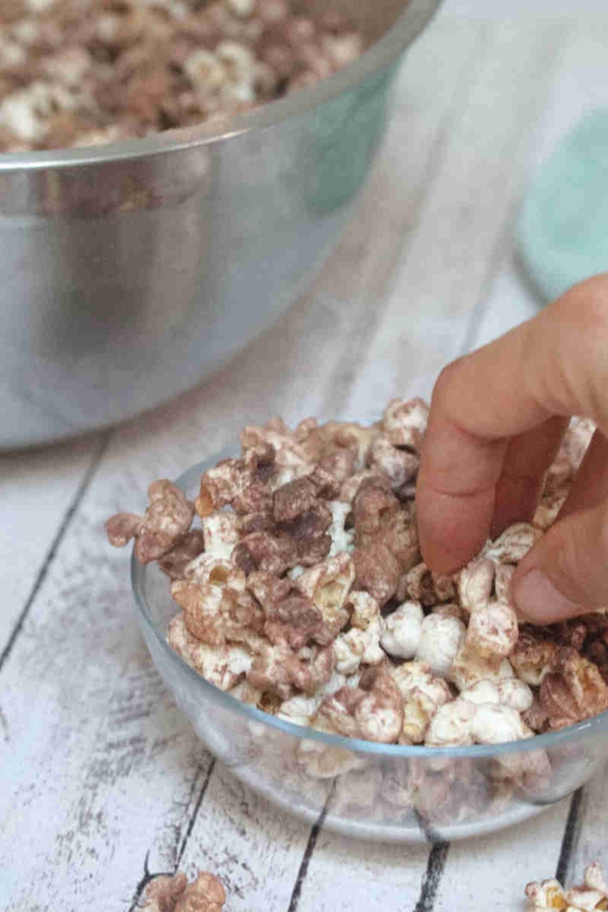 Hand grabbing chocolate protein popcorn out of a glass bowl.