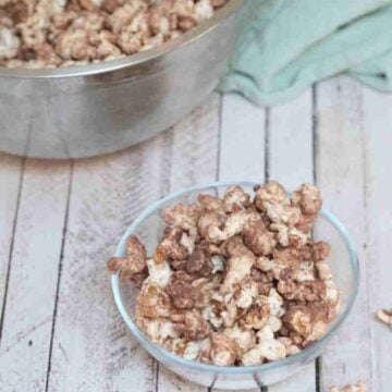 Chocolate protein powder popcorn in a glass bowl with more popcorn in a large bowl behind it.