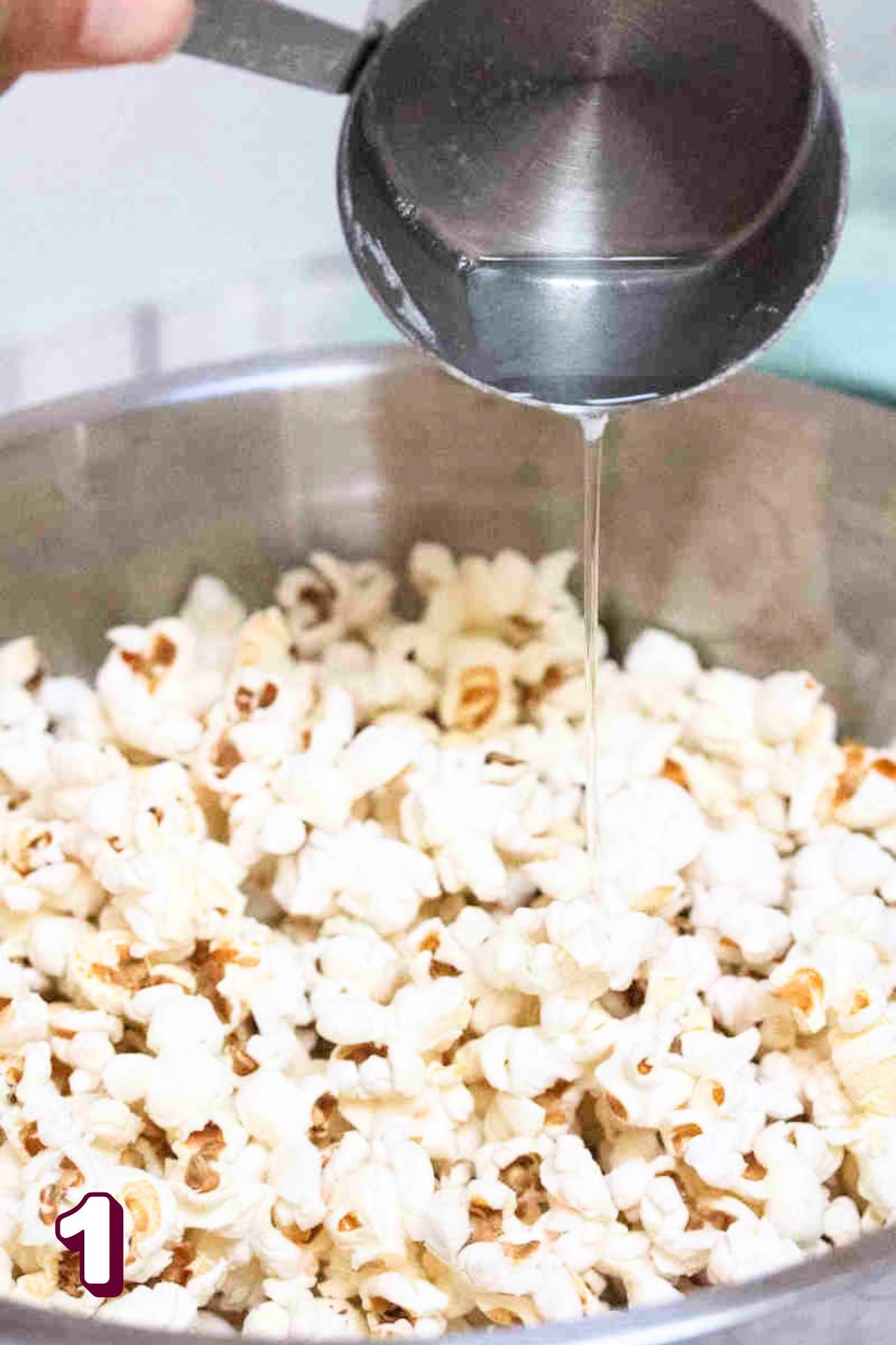 Coconut oil being poured into a bowl of poppcorn.