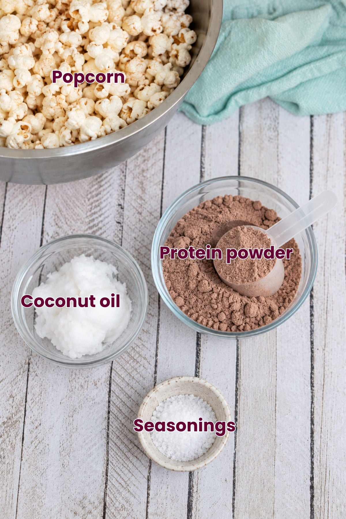 Coconut oil, popcorn, protein powder, and salt in a bowl with text labels over the top.
