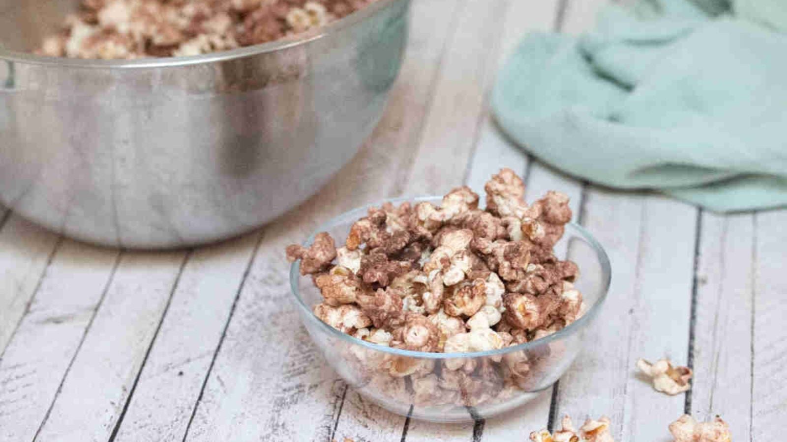 Chocolate protein powder popcorn in a glass bowl with more popcorn in a large bowl behind it.